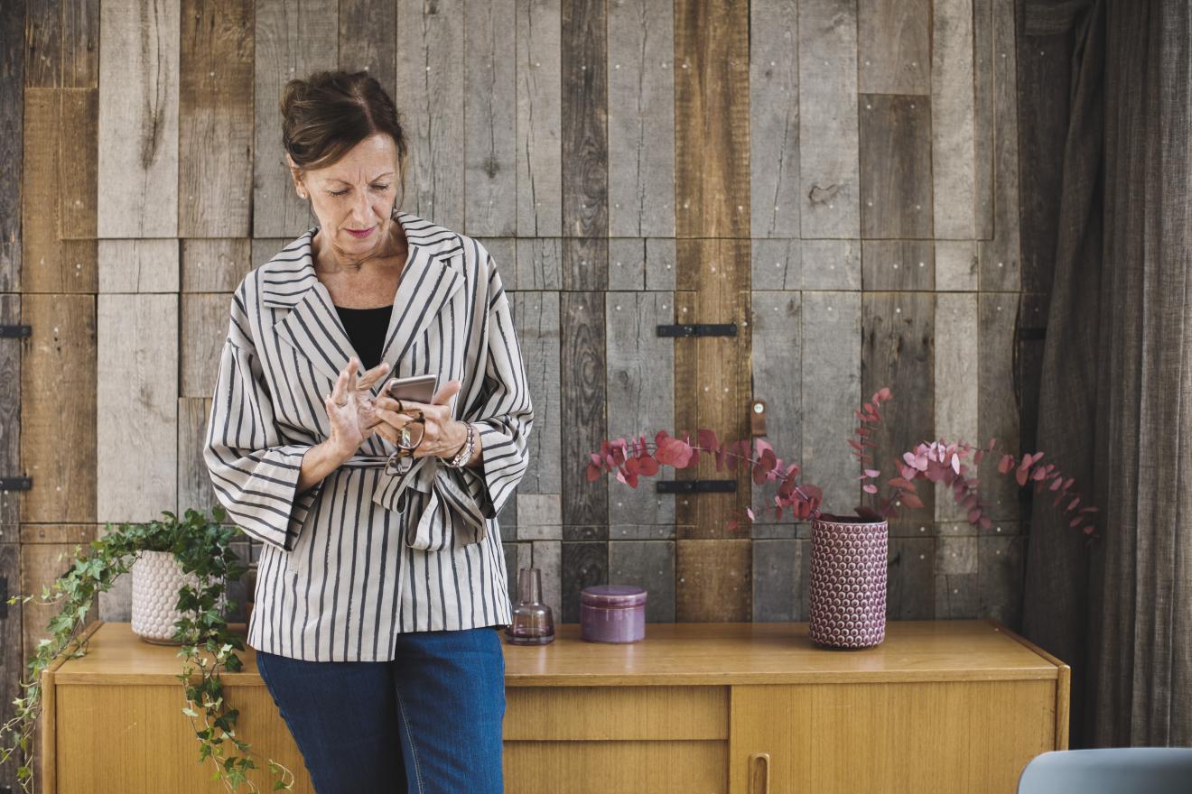 Photo of an older woman in a wood paneled office looking down at her mobile phone to view short codes information.