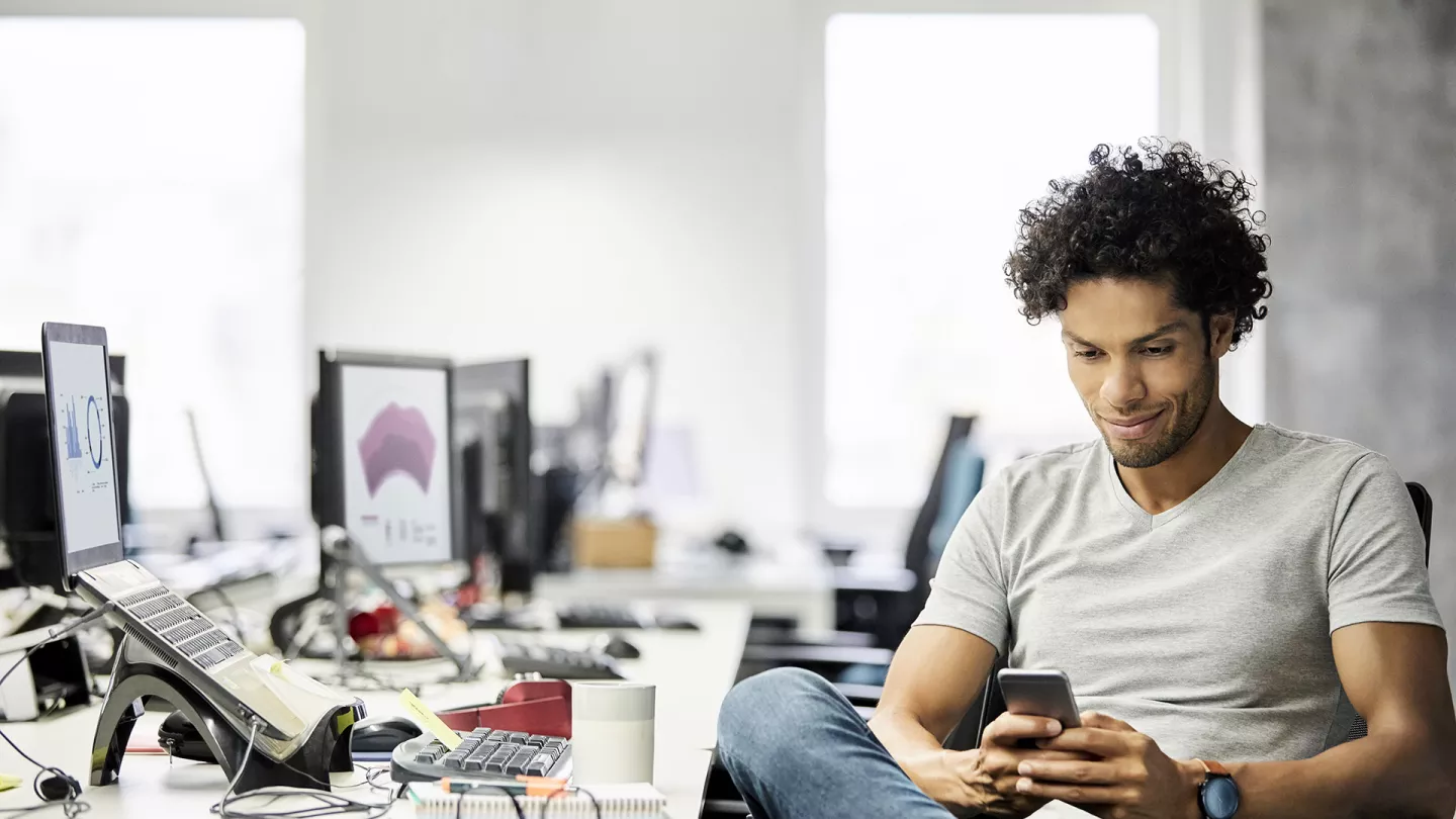 Image of a man at a computer looking at his phone