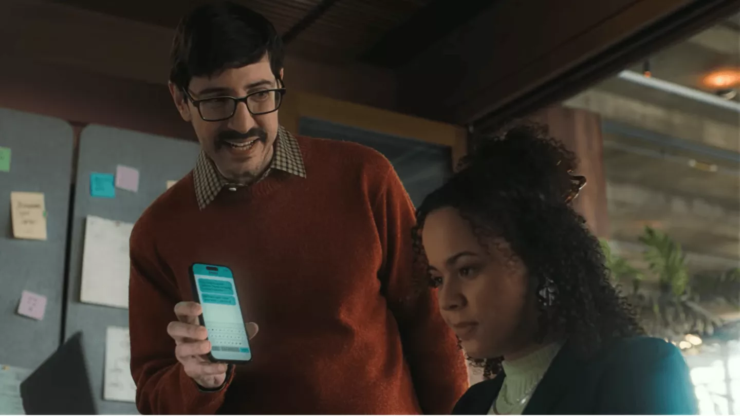 Image of a man holding a phone up to a woman showing her how shortcodes work